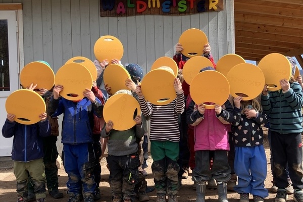 Kinder mit den Sitzkissen vor dem Gesicht 